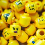 Verschillende gele LEGO-hoofdjes met blije, boze en verbaasde gezichtsuitdrukkingen als metafoor voor emoties